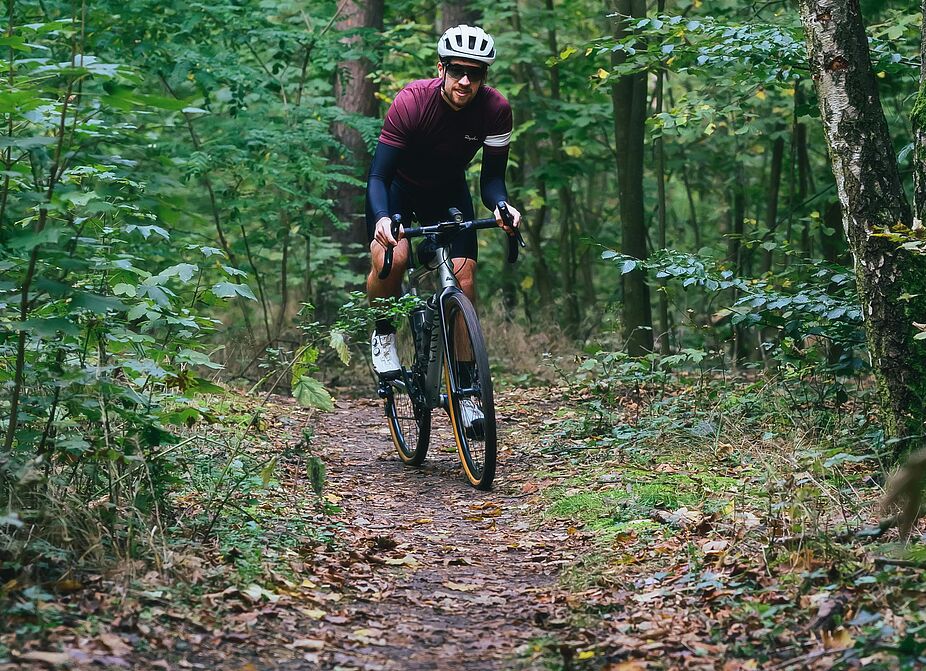 Gravelbiker im Wald Ein Gravelbiker fährt auf einem schmalen Waldpfad.
