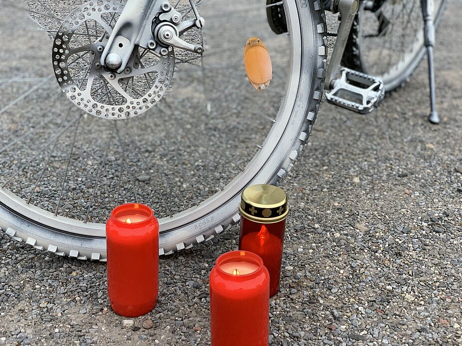 Ride of Silence Drei rote Grabkerzen in Nahaufnahme vor dem Vorderrad eines weiß angestrichenen Ghost-Bikes zur Erinnerung an Unfallopfer