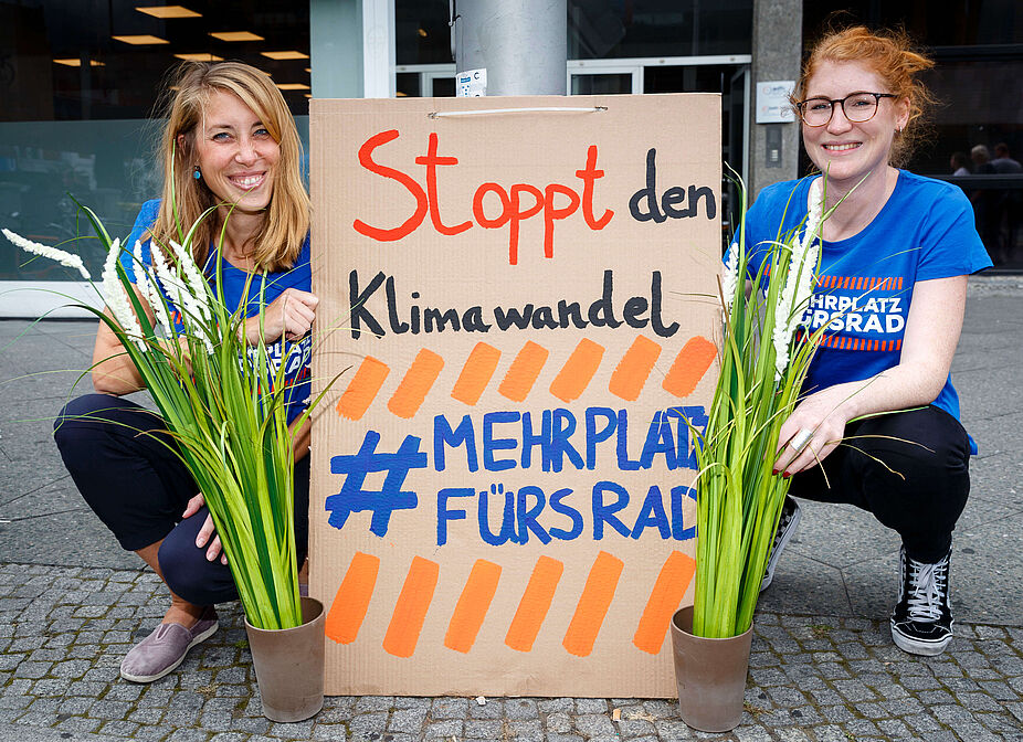 Demo „Stoppt den Klimawandel – Mehr Platz fürs Rad“ Zwei Frauen knien neben Plakat mit Aufschrift "Stoppt den Klimawandel #MehrPlatzFürsRad"